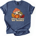 Small Things Big Thanks Comfort Colors T-shirt in Heather Navy, laid flat. A red gingham mushroom and a green polka-dot mushroom in a stitched patchwork style sit behind a pumpkin, an acorn and autumn leaves above the words Small Things Big Thanks. Sleeves rolled, on white.