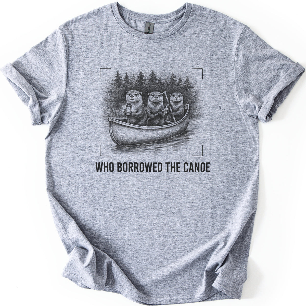 Who Borrowed The Canoe Comfort Colors T-shirt in Sport Grey, laid flat. A black pencil-style sketch of three otters in a canoe before pine trees, one holding a lantern and two holding paddles, inside corner brackets above the words WHO BORROWED THE CANOE. Sleeves rolled, on white.