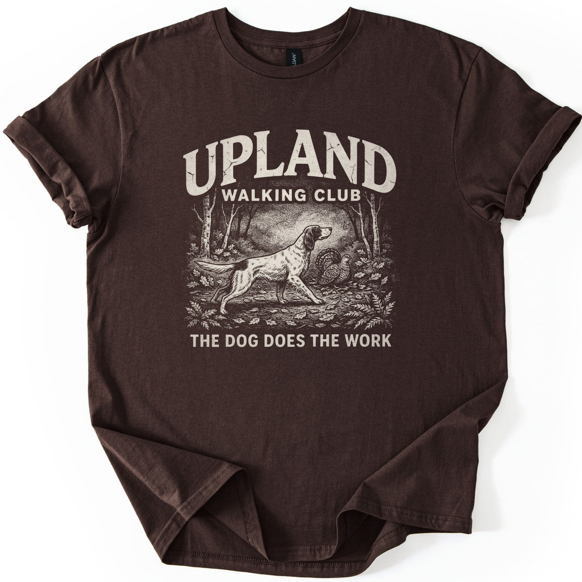 Upland Walking Club Comfort Colors T-shirt in Dark Chocolate, laid flat. A cream vintage-style print shows a setter dog stalking a grouse in a leafy forest, below the words Upland Walking Club and above The Dog Does The Work. Sleeves are rolled, on a white background.