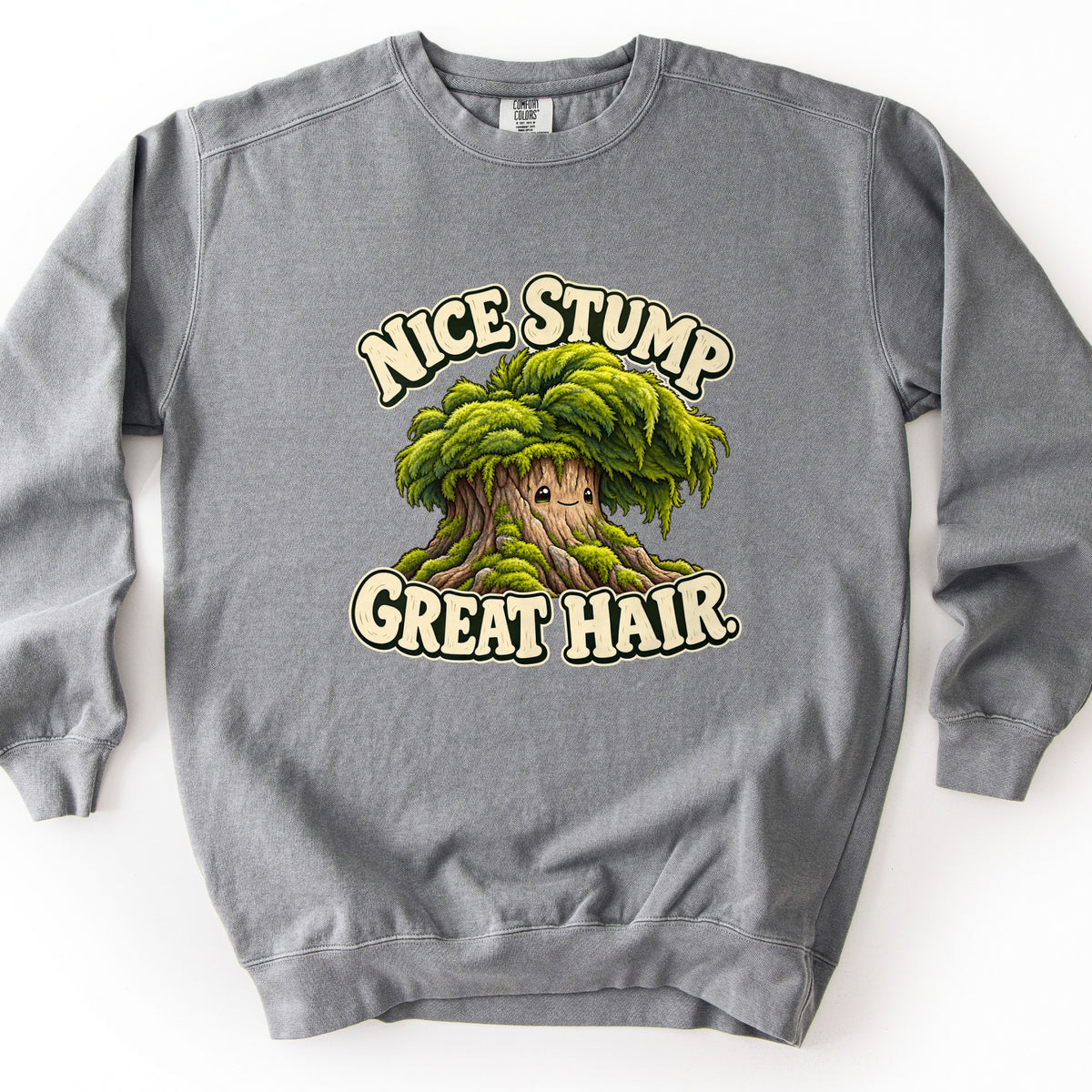 Nice Stump Great Hair Comfort Colors crewneck sweatshirt in Grey, laid flat. A cartoon tree stump with a small smiling face and a thick mop of green moss for hair sits between the words Nice Stump above and Great Hair. below, in cream bubble letters. The sweatshirt lies on a white background.