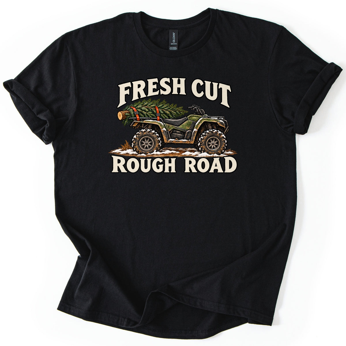Fresh Cut Rough Road Comfort Colors T-shirt in Black, laid flat. A muddy green camo ATV with a cut evergreen tree strapped to its rear rack sits on snowy dirt between the cream words Fresh Cut and Rough Road. The sleeves are cuffed, on a white background.