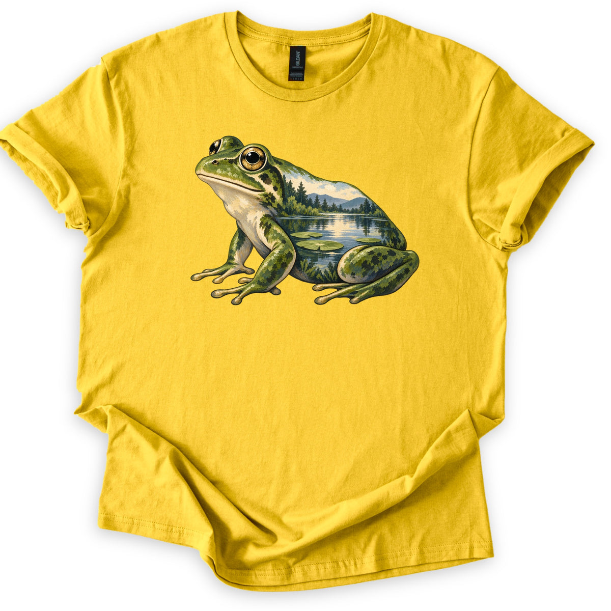 Lily Pond Frog Comfort Colors T-shirt in Daisy, laid flat. A painted green frog sits in profile, its body filled with a lake scene of pine trees, mountains and lily pads. No words are printed. The shirt has cuffed sleeves on a white background.