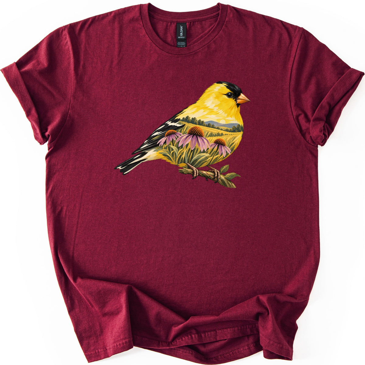 Goldfinch Meadow Comfort Colors T-shirt in Maroon, laid flat. A yellow goldfinch with a black cap and black-and-white wings perches on a branch, its body filled with a meadow of purple coneflowers, grass and distant hills. No words. Sleeves rolled, on white.