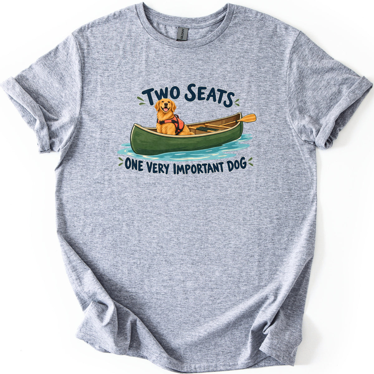 Important Dog Comfort Colors T-shirt in Sport Grey, laid flat. A golden retriever in an orange life vest sits in a green canoe with a paddle on blue water, between the words Two Seats and One Very Important Dog. The shirt lies on a white background with cuffed sleeves.