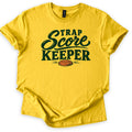 Trap Score Keeper Comfort Colors T-shirt in Daisy, laid flat. Dark green lettering reads Trap Score Keeper, with Score in flowing script above an orange clay target with motion lines. The sleeves are cuffed and it lies on a plain white background.