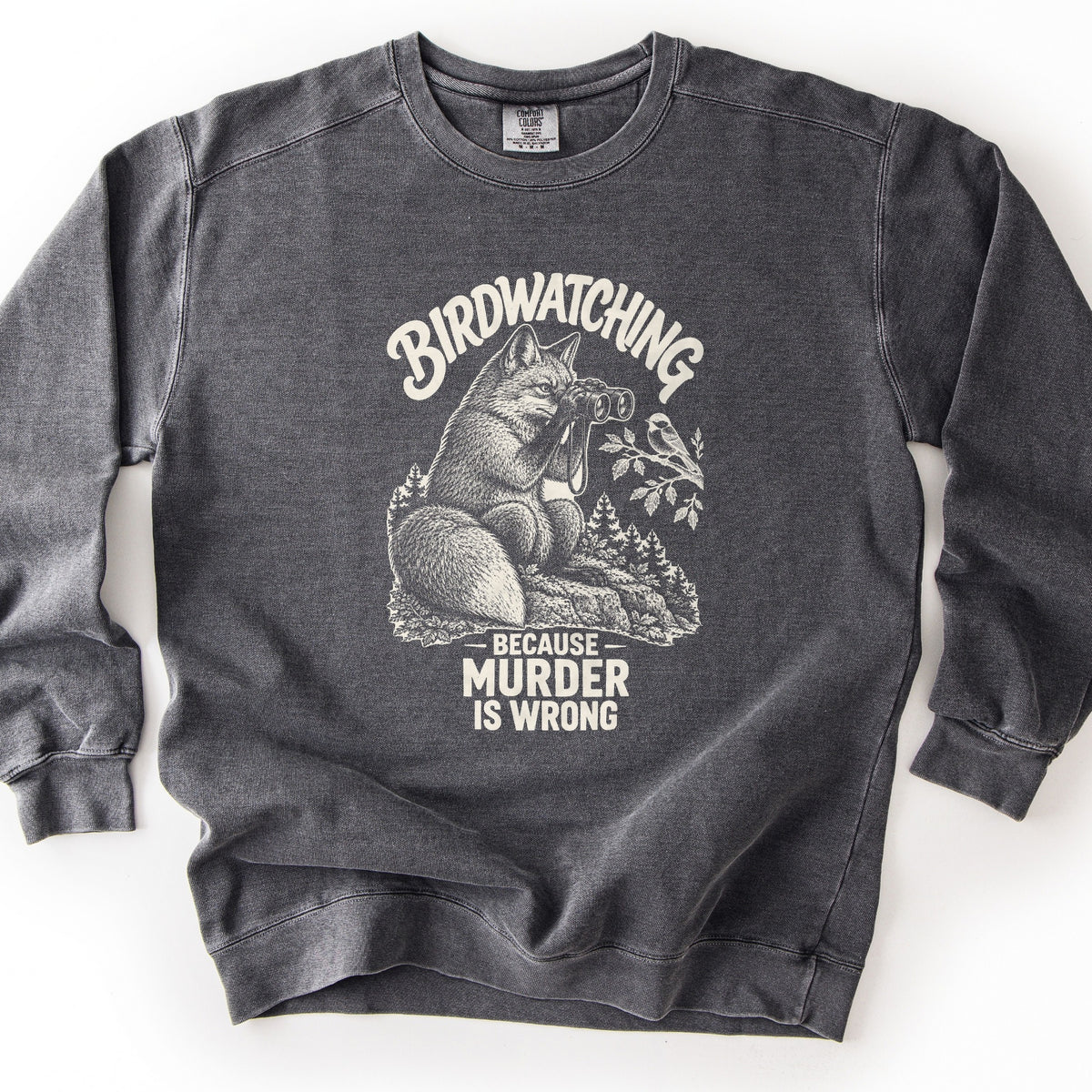Birdwatching Because Murder Is Wrong Comfort Colors crewneck sweatshirt in Pepper, laid flat. A cream sketch of a fox on a rock using binoculars to watch a small bird on a leafy branch, with pine trees behind. Birdwatching arches above; Because Murder Is Wrong is below. White background.
