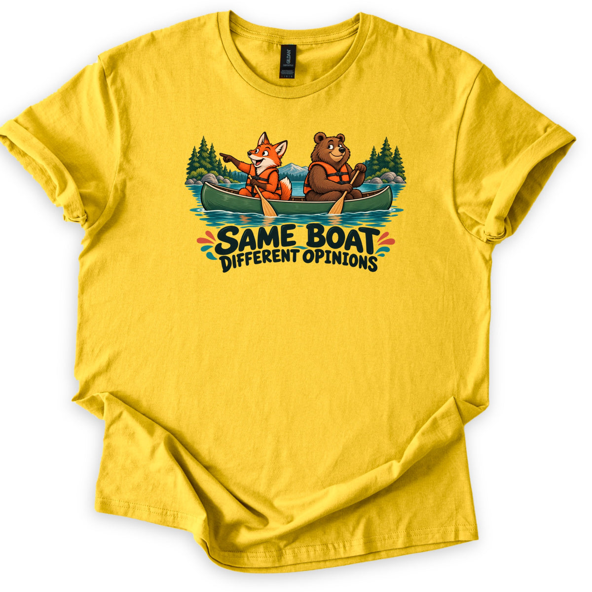 Same Boat Different Opinions Comfort Colors T-shirt in Daisy, laid flat. A cartoon fox pointing ahead and a brown bear paddling, both in life vests, sit in a green canoe on a pine-lined lake above the words Same Boat Different Opinions. The shirt lies on a white background.