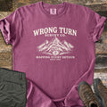 Wrong Turn Survey Co Comfort Colors T-shirt in Berry, laid flat. Cream print of the words Wrong Turn Survey Co. above snowy mountains with a winding trail leading to a compass, then Mapping Every Detour, Since 1985. Shown on wood boards with olive pants and brown hiking boots.