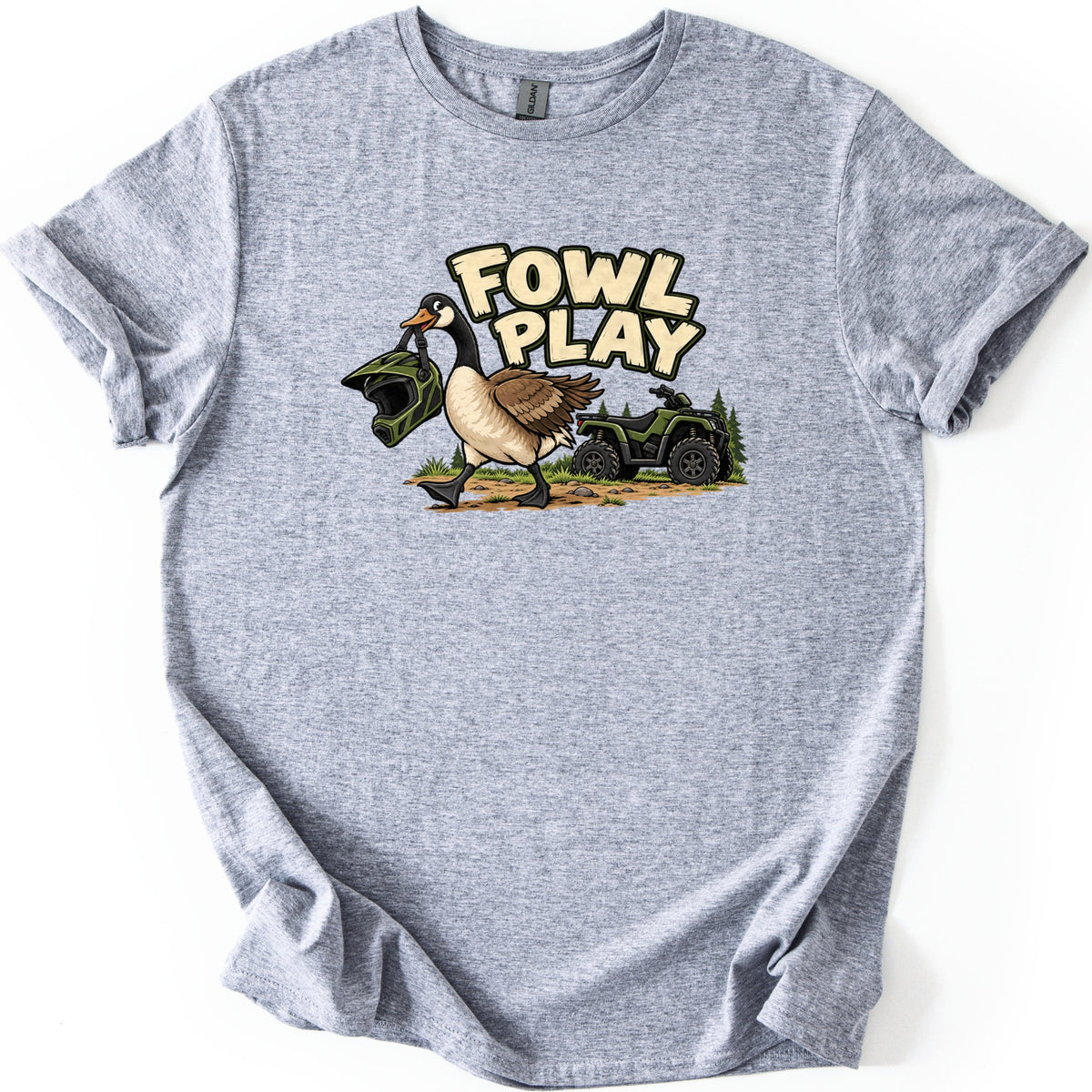 Fowl Play Comfort Colors T-shirt in Sport Grey, laid flat. A cartoon Canada goose carries a green motocross helmet in its beak past a green ATV and pine trees, below the words Fowl Play. The shirt lies on a white background with cuffed sleeves.