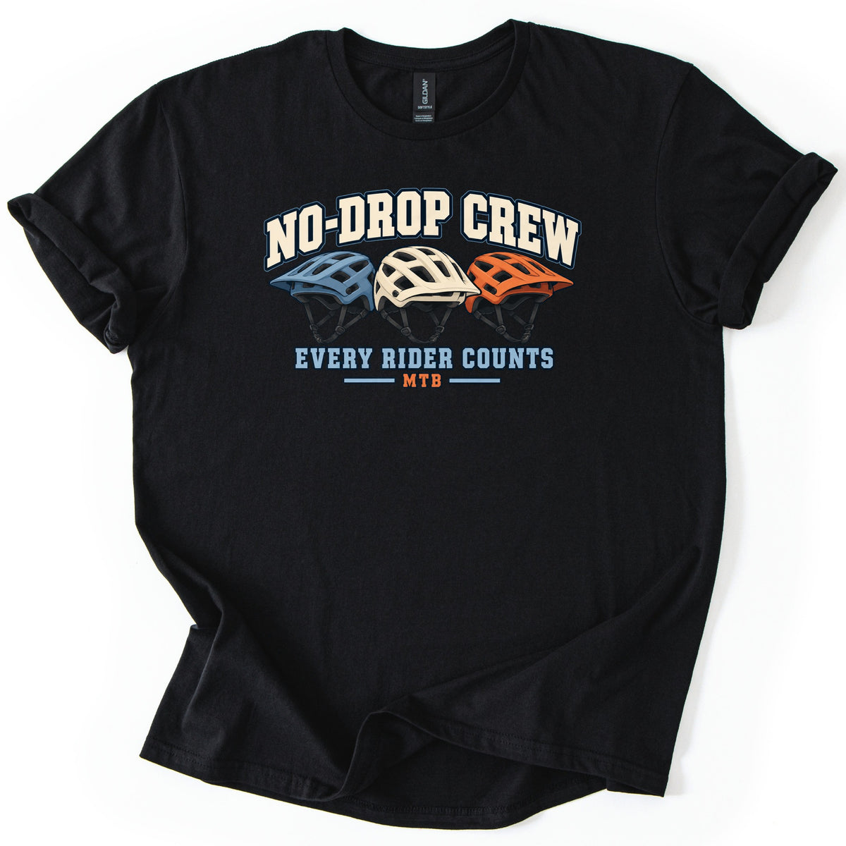 No Drop Crew Comfort Colors T-shirt in Black, laid flat. Three mountain bike helmets in blue, cream and orange sit under the arched words No-Drop Crew, with Every Rider Counts and MTB below. The shirt has rolled sleeves on a white background.