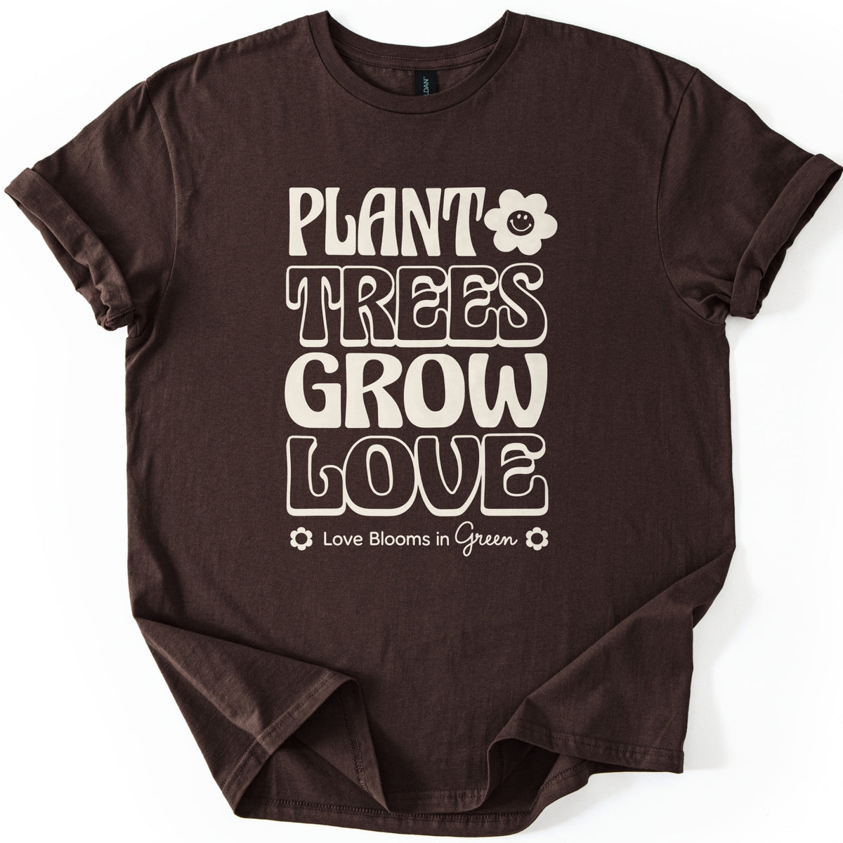 Plant Trees Grow Love Comfort Colors T-shirt in Dark Chocolate, laid flat. Cream retro bubble letters read Plant Trees Grow Love, with a smiling daisy beside Plant and Love Blooms in Green between two small flowers below. Sleeves are rolled on a white background.