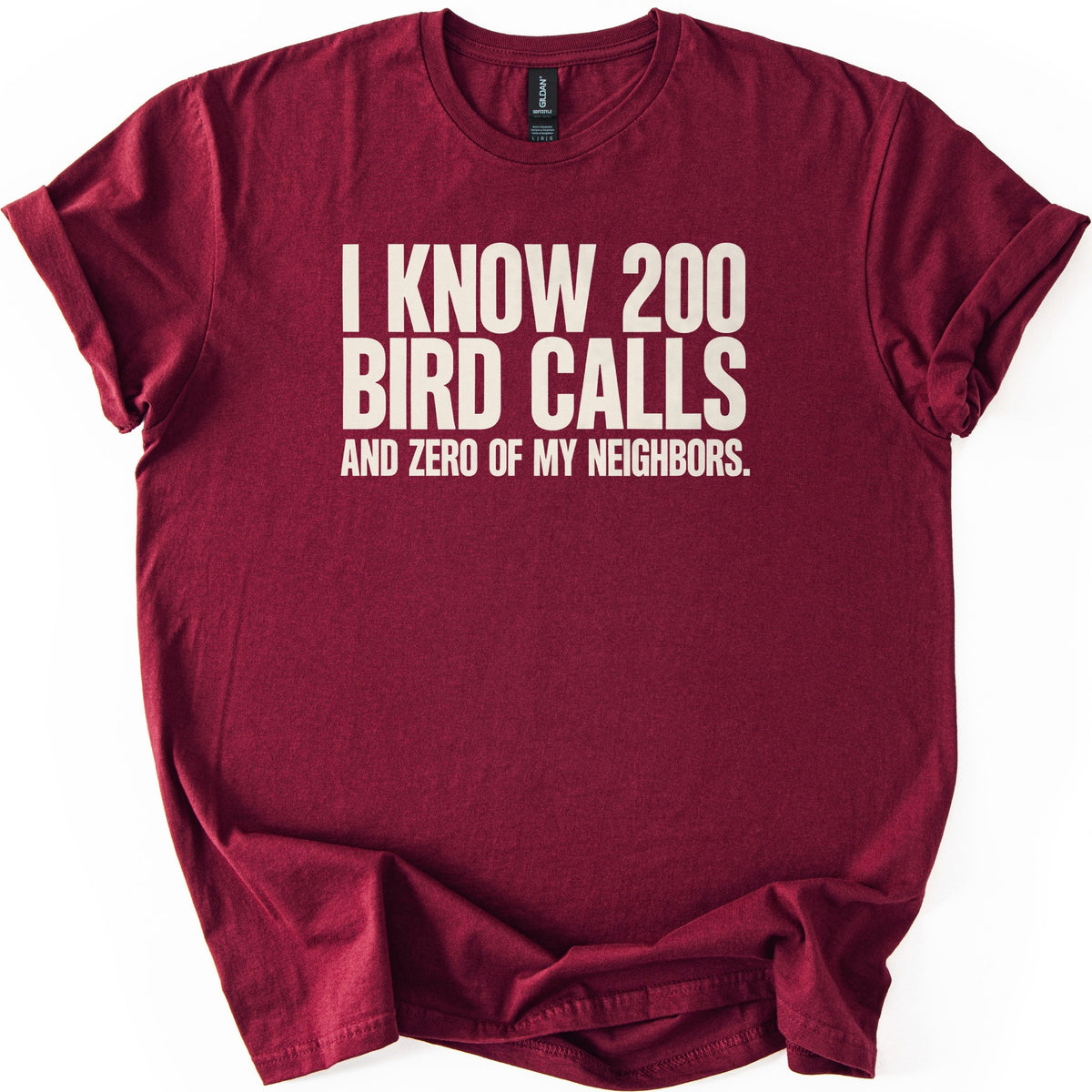 I Know 200 Bird Calls and Zero of My Neighbors Comfort Colors T-shirt in Maroon, laid flat. Bold cream capital letters across the chest read I Know 200 Bird Calls and Zero of My Neighbors. The shirt lies on a white background with rolled sleeves and a loosely rumpled hem.