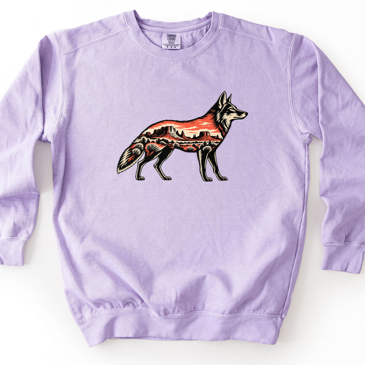 Desert Mesa Coyote Comfort Colors crewneck sweatshirt in Orchid, laid flat. A coyote in profile filled with a desert scene of red mesas, a sunset sky and sagebrush, with no words printed. The sweatshirt lies on a plain white surface with sleeves spread out at the sides.