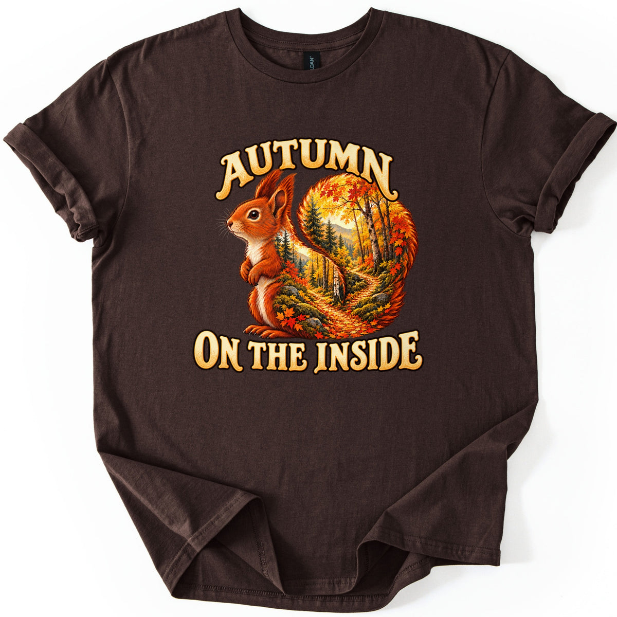 Autumn on the Inside Comfort Colors T-shirt in Dark Chocolate, laid flat. A red squirrel whose curled tail holds an autumn forest scene with a leaf-covered path sits between the words Autumn and On the Inside. The shirt has rolled sleeves on a white background.