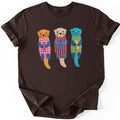 Patchwork Otter Comfort Colors T-shirt in Dark Chocolate, laid flat. Three fabric-patch otters with stitched X eyes float side by side, each hugging a fish: orange in pink gingham, beige in purple and orange stripes, turquoise in yellow gingham. No words. Sleeves cuffed on a white surface.