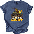 Tail Light Comfort Colors T-shirt in Heather Navy, laid flat. A cartoon firefly in a green helmet rides a muddy green ATV, its glowing yellow tail lit up, above the words Tail Light. The shirt lies on a white background with the sleeves rolled.