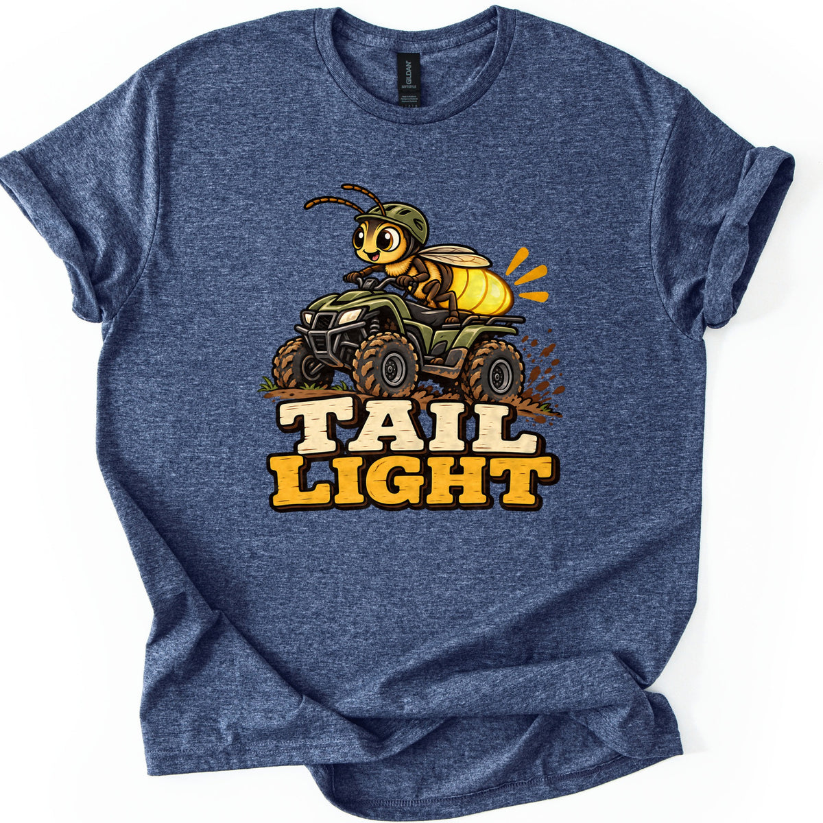 Tail Light Comfort Colors T-shirt in Heather Navy, laid flat. A cartoon firefly in a green helmet rides a muddy green ATV, its glowing yellow tail lit up, above the words Tail Light. The shirt lies on a white background with the sleeves rolled.