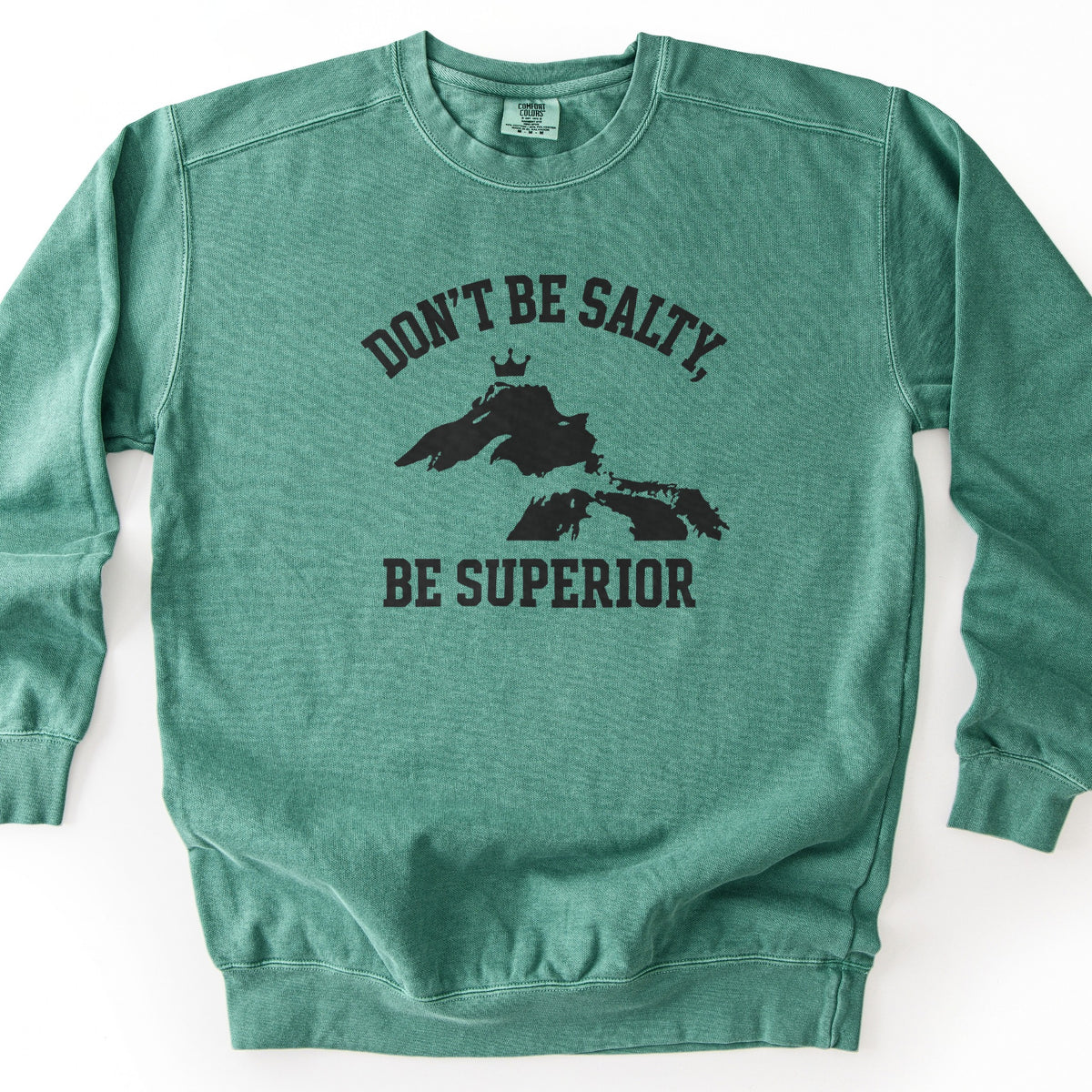 Be Superior Comfort Colors crewneck sweatshirt in Light Green, laid flat. Black print of the words Don't Be Salty, arched above a silhouette of Lake Superior topped with a small crown, with Be Superior below. Laid on a white background.