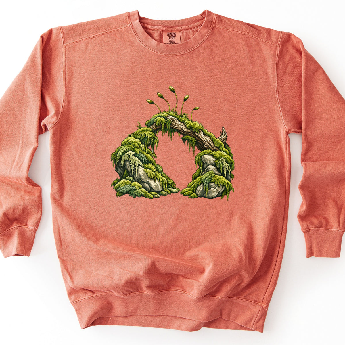 Moss Arch Comfort Colors crewneck sweatshirt in Terracotta, laid flat. A natural arch of mossy gray rocks joined by a weathered branch, covered in green moss and ferns with moss spore stalks sprouting on top; no words. Shown flat on a white background.