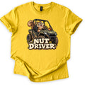 Nut Driver Comfort Colors T-shirt in Daisy, laid flat. A grinning cartoon squirrel drives a muddy camo side-by-side UTV over rocks and grass, an acorn on the hood, above the words Nut Driver in cream letters. The shirt lies on a plain white background.
