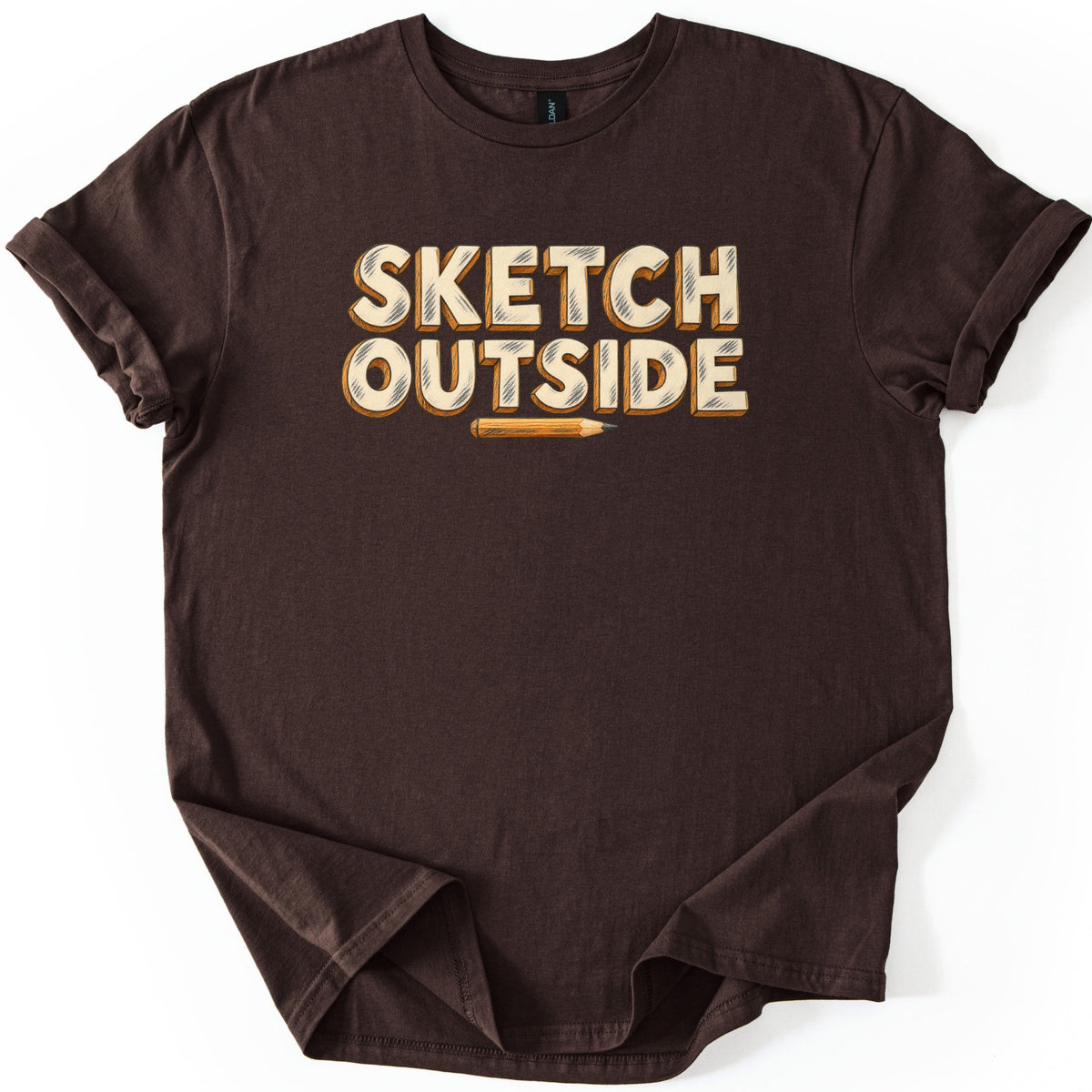 Sketch Outside Comfort Colors T-shirt in Dark Chocolate, laid flat. Cream block letters with orange 3D shadows and pencil-hatch shading spell Sketch Outside above a small sharpened pencil. The shirt has rolled sleeves and lies on a plain white background.