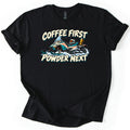 Coffee First Powder Next Comfort Colors T-shirt in Black, laid flat. A teal and cream cartoon snowmobile kicks up snow, with a helmet on the seat and a thermos on the back, between the words Coffee First Powder Next. Sleeves are rolled on a white background.