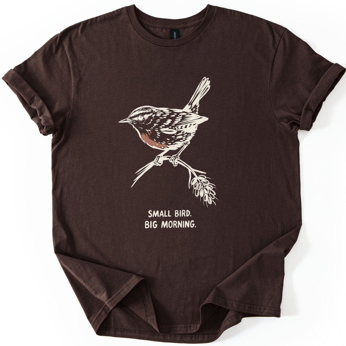 Small Bird Big Morning Comfort Colors T-shirt in Dark Chocolate, laid flat. A cream sketch of a wren with a rust-colored breast perches on a twig with a seed head, above the words Small Bird. Big Morning. The sleeves are rolled up, on a white background.