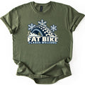 Fat Bike Flakes Welcome Comfort Colors T-shirt in Military Green, laid flat. A chunky knobby fat bike tire half buried in snow, with three snowflakes above it, sits over the words FAT BIKE FLAKES WELCOME. The shirt has rolled sleeves and lies on a white background.
