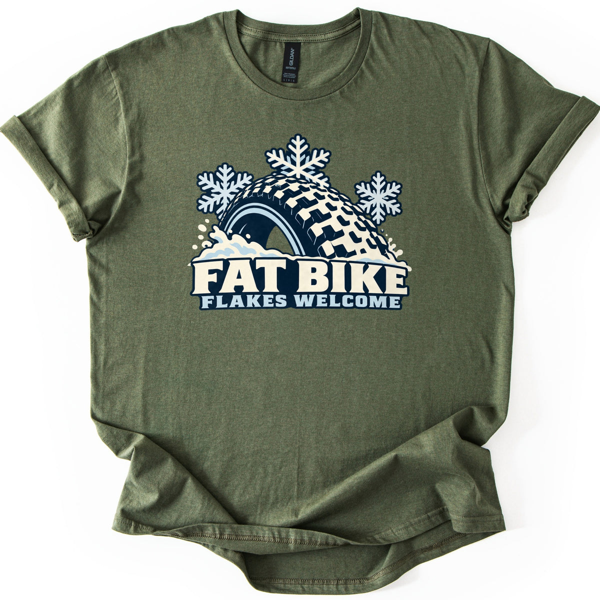 Fat Bike Flakes Welcome Comfort Colors T-shirt in Military Green, laid flat. A chunky knobby fat bike tire half buried in snow, with three snowflakes above it, sits over the words FAT BIKE FLAKES WELCOME. The shirt has rolled sleeves and lies on a white background.