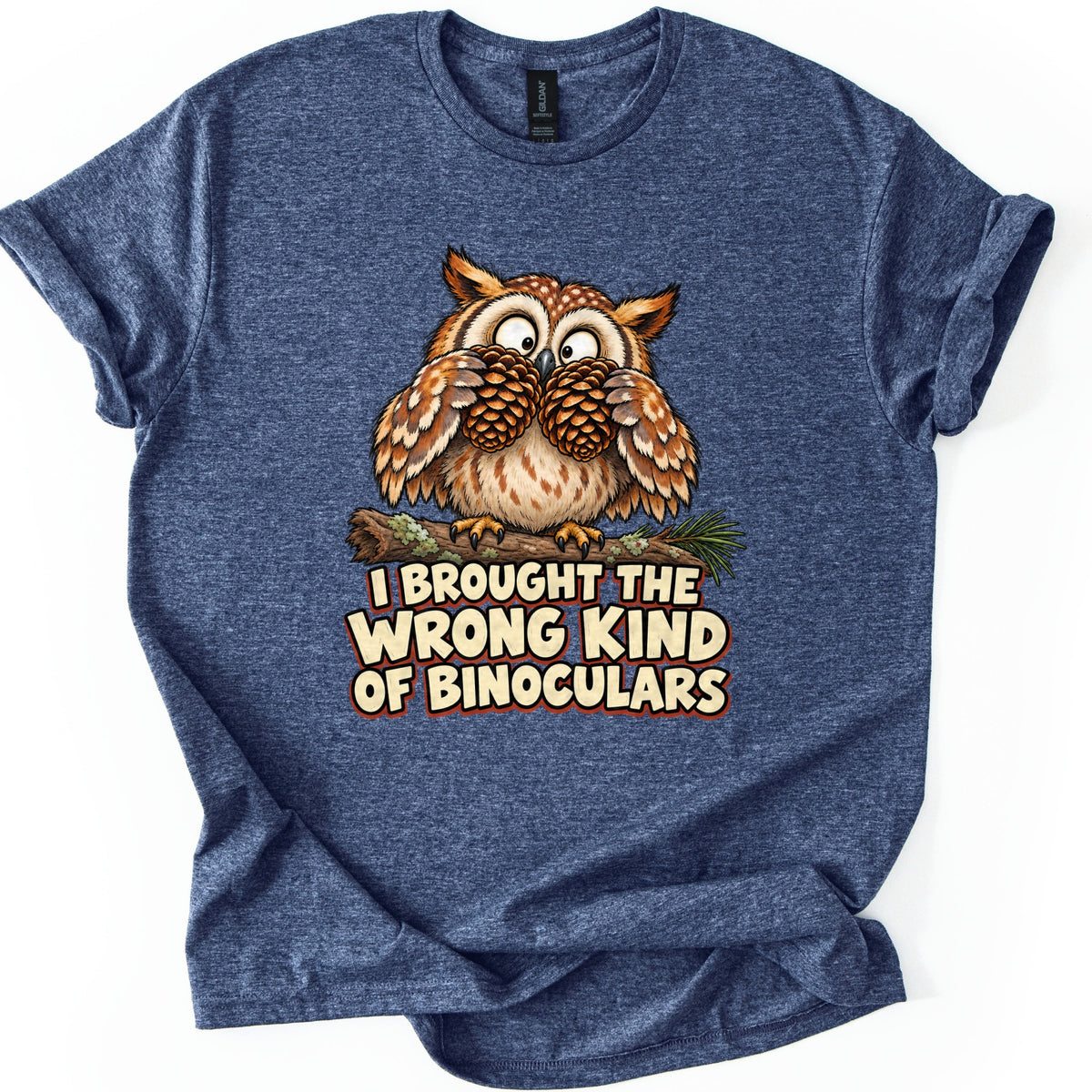 I Brought The Wrong Kind Of Binoculars Comfort Colors T-shirt in Heather Navy, laid flat. A wide-eyed cartoon owl on a mossy branch holds two pine cones to its eyes like binoculars, above the words I Brought The Wrong Kind Of Binoculars in cream letters. Sleeves are rolled up on a white background.