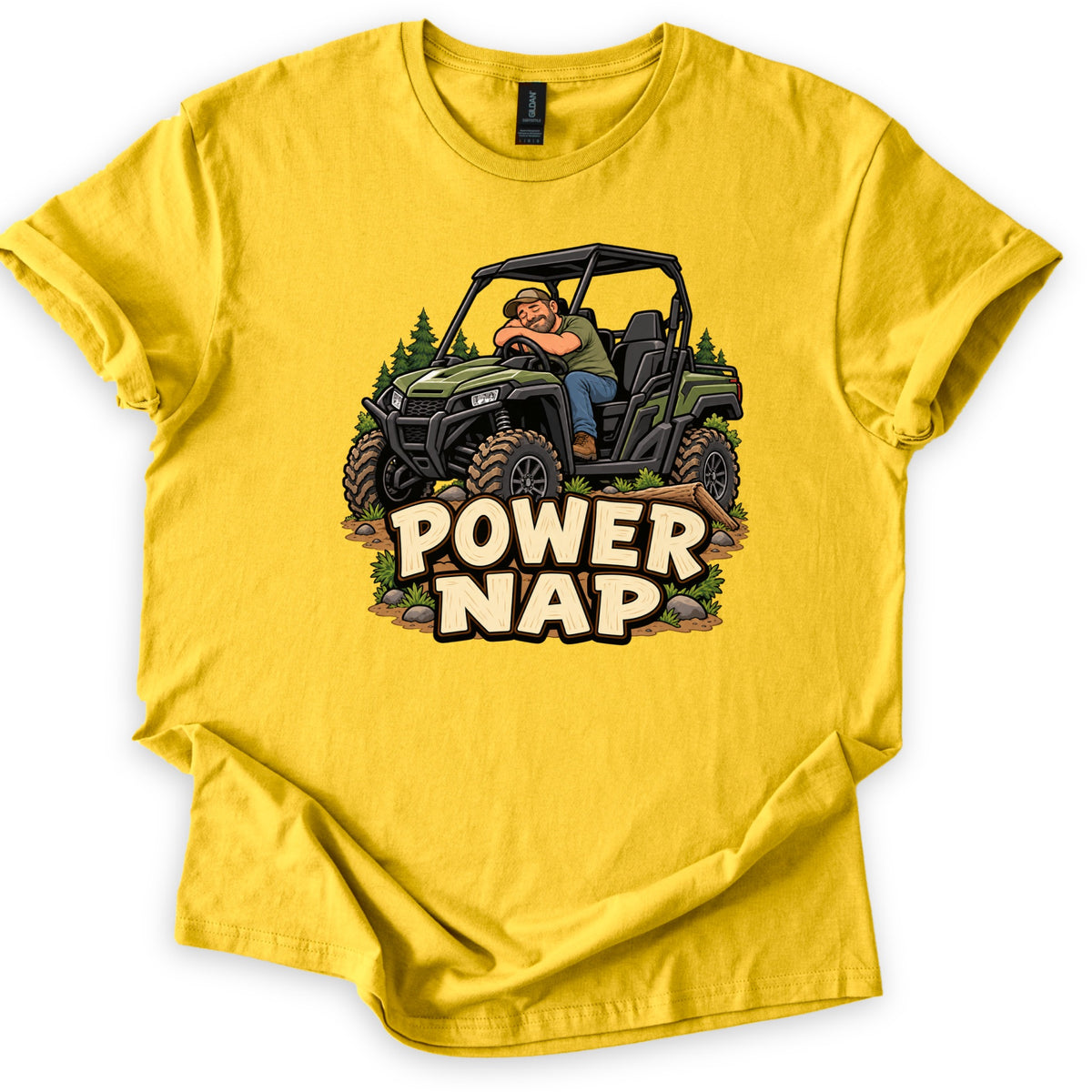 Power Nap Comfort Colors T-shirt in Daisy, laid flat. A cartoon man in a cap sleeps slumped over the wheel of a green side-by-side UTV among pine trees, above the words Power Nap in cream letters. The shirt lies on a white background with sleeves cuffed.