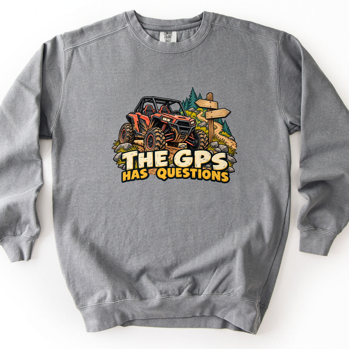 The GPS Has Questions Comfort Colors crewneck sweatshirt in Grey, laid flat. A cartoon orange side-by-side off-road vehicle splattered with mud climbs a rocky dirt trail past a wooden signpost and pine trees, above the words The GPS Has Questions. Laid on a white surface.