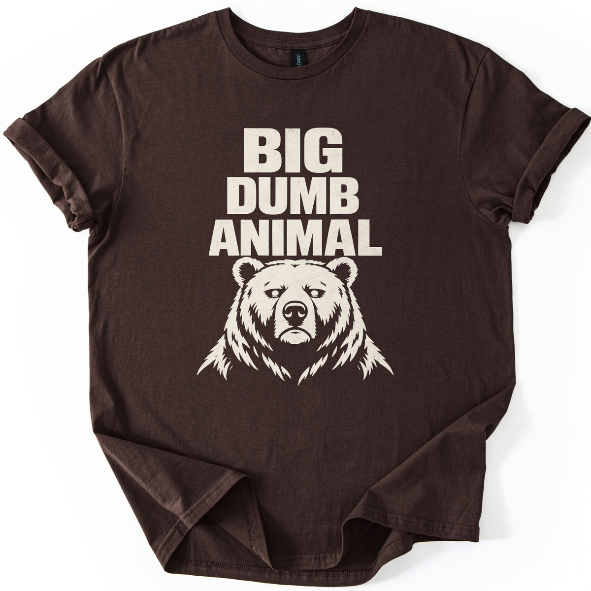 Big Dumb Animal Comfort Colors T-shirt in Dark Chocolate, laid flat. Bold cream letters read BIG DUMB ANIMAL above a cream illustration of a stern, front-facing bear head with shaggy fur. The sleeves are rolled and the shirt lies on a white background.
