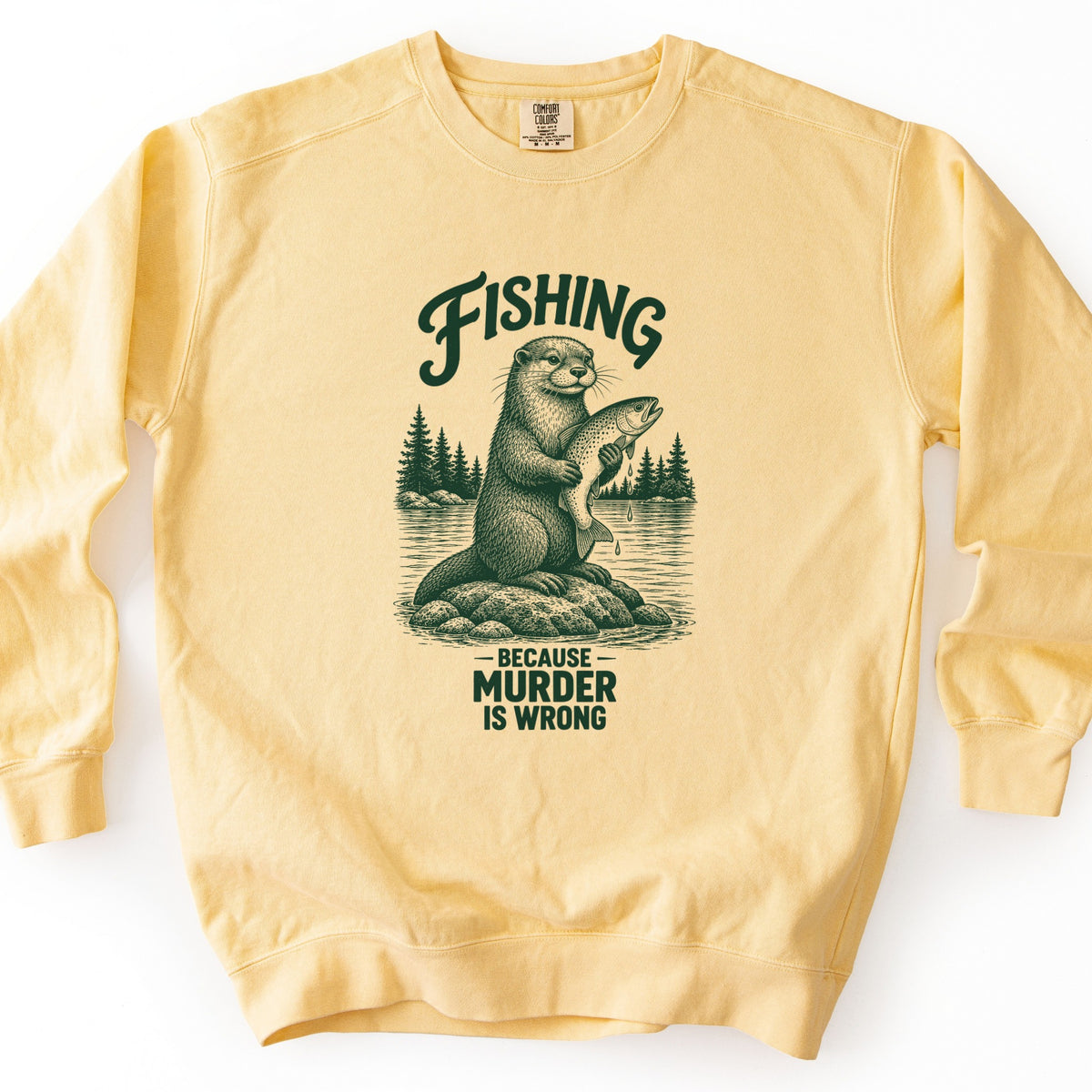 Fishing Because Murder Is Wrong Comfort Colors crewneck sweatshirt in Butter, laid flat. A dark green etched otter perches on a lake rock clutching a dripping trout, with pine trees behind it. The word Fishing curves above it and Because Murder Is Wrong sits below. Laid on a white surface.
