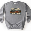 Stuck Together Comfort Colors crewneck sweatshirt in Grey, laid flat. Two teal ATVs covered in mud, one towing the other with an orange strap, between the words Stuck Together in cream distressed lettering. Shown on a white background.