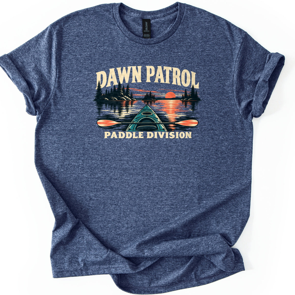 Dawn Patrol Paddle Division Comfort Colors T-shirt in Heather Navy, laid flat. The words Dawn Patrol arch over a kayak bow and paddle on a lake with pine-tree islands and an orange sunset reflected on the water, above the words Paddle Division. Sleeves cuffed, on a white background.