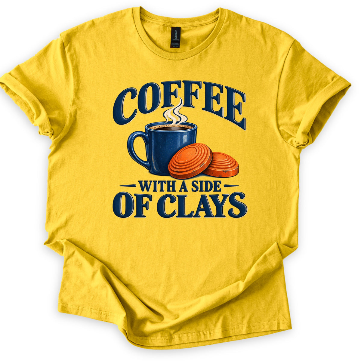 Coffee with a Side of Clays Comfort Colors T-shirt in Daisy, laid flat. A steaming navy enamel mug of coffee sits beside two orange clay targets, with the words COFFEE above and WITH A SIDE OF CLAYS below in navy. The shirt lies on a white background with cuffed sleeves.