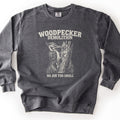 Woodpecker Demolition Comfort Colors crewneck sweatshirt in Pepper, laid flat. An etched-style drawing of a pileated woodpecker chipping splinters from a broken tree trunk, between the words Woodpecker Demolition and No Job Too Small in off-white. Shown on a plain white surface.