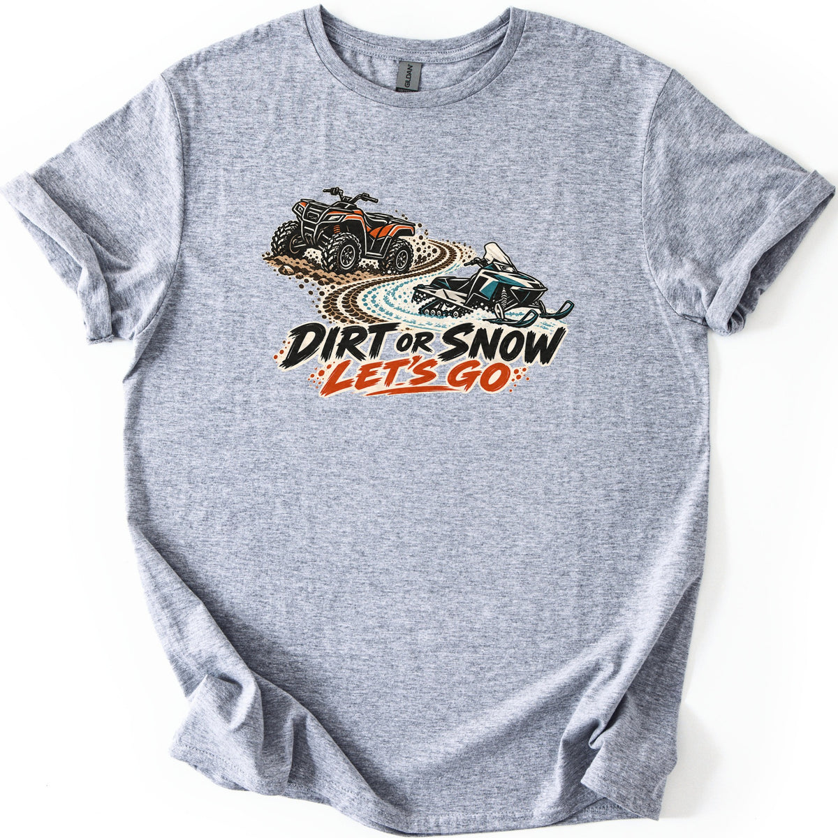 Dirt or Snow Let's Go Comfort Colors T-shirt in Sport Grey, laid flat. An orange ATV on a dirt trail curves into a snowy track with a teal snowmobile, above the words DIRT OR SNOW LET'S GO. The shirt lies on a white background with cuffed sleeves.