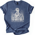 The Waterfowler Comfort Colors T-shirt in Heather Navy, laid flat. A white engraving-style drawing of a mallard duck in a camo shirt with a duck call on a lanyard, set in tall marsh grass inside a thin frame, above the words THE WATERFOWLER. Sleeves cuffed, on white.