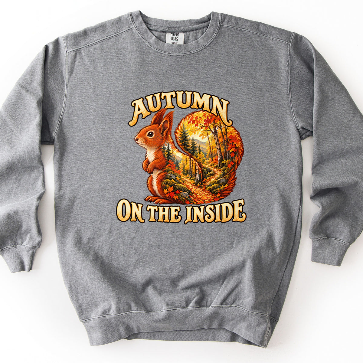 Autumn on the Inside Comfort Colors crewneck sweatshirt in Grey, laid flat. A red squirrel whose tail is filled with an autumn forest trail scene sits between the words Autumn on the Inside in cream lettering. Shown on a white background.