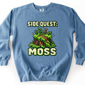 Side Quest Moss Comfort Colors crewneck sweatshirt in Blue Jean, laid flat. Pixel-art tree stump covered in green moss and small ferns, with two orange-tipped sprouts and sparkles, between the words Side Quest: and Moss in mossy cream pixel letters. Shown on a white background.