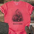 Who Ate My Worms Comfort Colors T-shirt in Watermelon, laid flat. A black sketch of a heron and an otter each eating a worm beside a mink and a spilled bait can, inside viewfinder corners, above the words Who Ate My Worms. Olive pants and brown hiking boots lie on weathered wood.