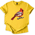 Winter Cardinal Comfort Colors T-shirt in Daisy, laid flat. A painted red cardinal perches on a snowy branch, its body filled with a winter scene of evergreens, a snowy path and red-berry bushes. No words are printed. The sleeves are cuffed on a white background.