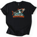 Follow the Water Home Comfort Colors T-shirt in Black, laid flat. A leaping orange salmon, its body filled with a pine forest and waterfall, rises from teal waves above the words Follow the Water Home. The shirt lies on a white background with its sleeves rolled.