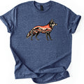 Desert Mesa Coyote Comfort Colors T-shirt in Heather Navy, laid flat. A standing coyote in profile, drawn in black and cream, has its body filled with a red desert scene of mesas, an orange sky and shrubs. No words are printed. The sleeves are rolled, on a white surface.
