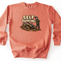 Self Parking Comfort Colors crewneck sweatshirt in Terracotta, laid flat. A cartoon rider in a helmet, green shirt and muddy pants stands with crossed arms beside a quad ATV stuck in mud, under the words Self Parking. Shown on a white background.