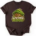 Living Roof Comfort Colors T-shirt in Dark Chocolate, laid flat. A cartoon tree-stump cottage with a thick green moss roof, an arched wooden door and a glowing window sits above the words Living Roof in cream and moss-green letters. Sleeves are cuffed on a white surface.