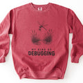 My Kind Of Debugging Comfort Colors crewneck sweatshirt in Crimson, laid flat. A black sketch-style drawing of a dragonfly catching a mosquito above a pond with cattails and lily pads, over the words My Kind Of Debugging. Laid on a white surface.