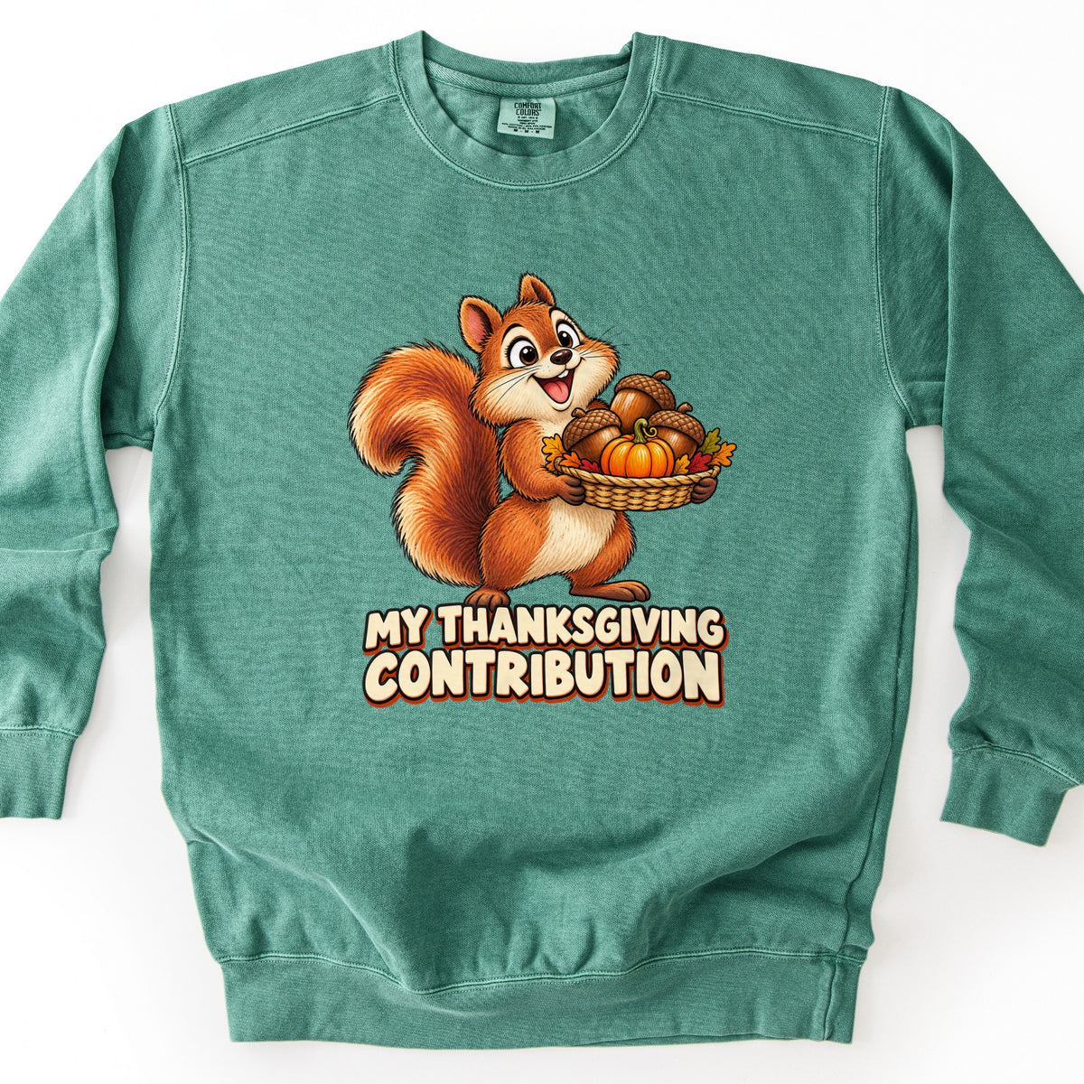 My Thanksgiving Contribution Comfort Colors crewneck sweatshirt in Light Green, laid flat. A smiling cartoon squirrel holds a woven basket of acorns, a small pumpkin, and autumn leaves above the words My Thanksgiving Contribution in cream letters. Shown on a plain white background.